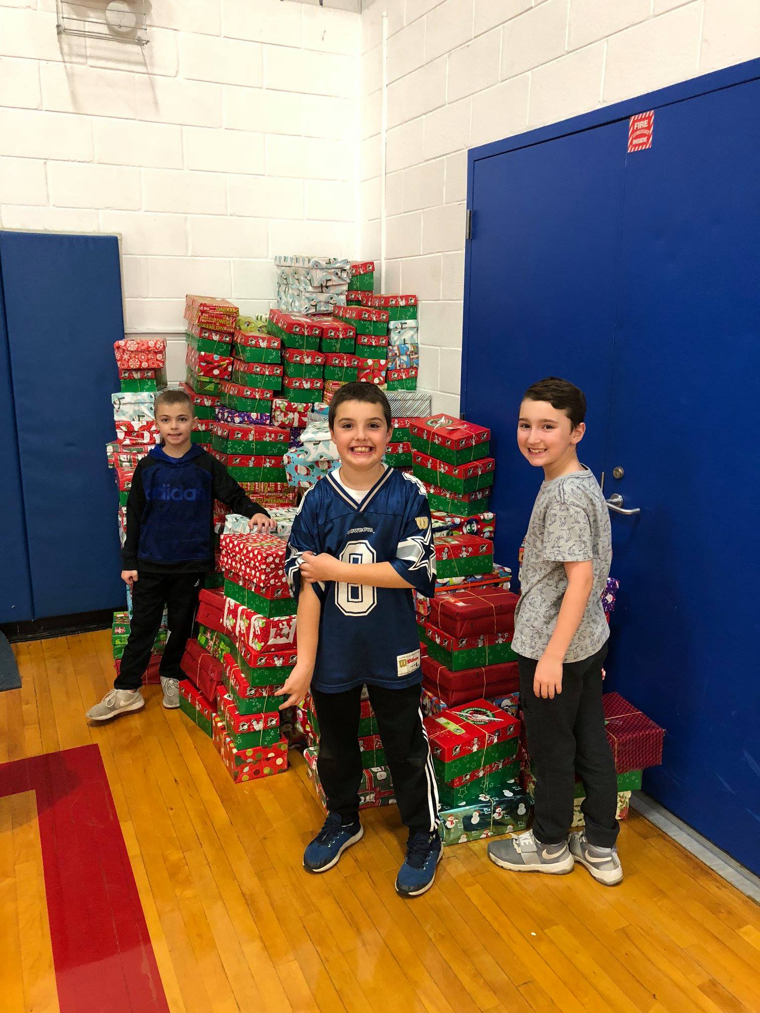 Operation Shoe Box Event - Three Children in front of a large pile of wrapped shoeboxes